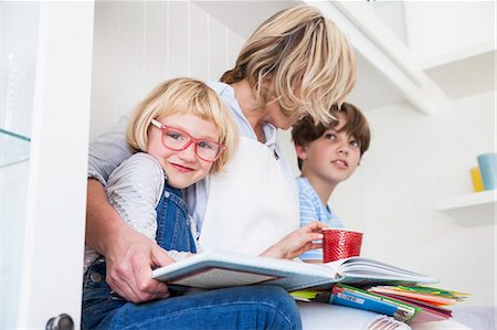 sitting in jeans - Mature woman sitting on kitchen counter reading storybooks with son and daughter Stock Photo - Premium Royalty-Free, Code: 649-08894314