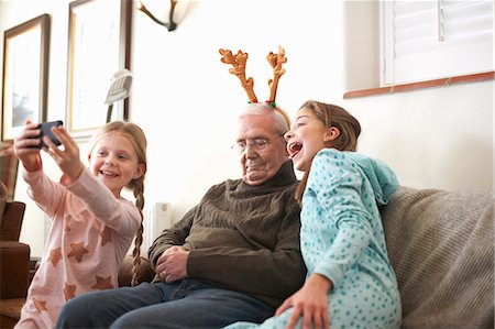 Sisters taking smartphone selfie of sleeping grandfather in reindeer antlers Stock Photo - Premium Royalty-Free, Code: 649-08894381