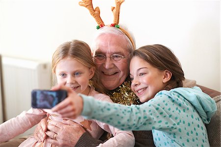 family at christmas - Sisters taking smartphone selfie with grandfather in reindeer antlers Foto de stock - Sin royalties Premium, Código: 649-08894382