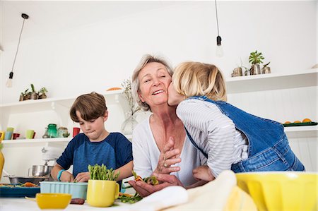 Girl kissing grandmother while preparing fresh vegetables at kitchen table Stock Photo - Premium Royalty-Free, Code: 649-08894892