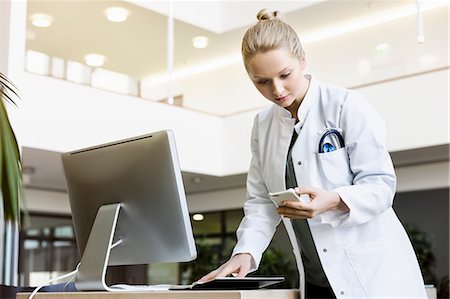 schedule - Doctor standing beside computer, holding open diary, looking at smartphone Stock Photo - Premium Royalty-Free, Code: 649-08900677