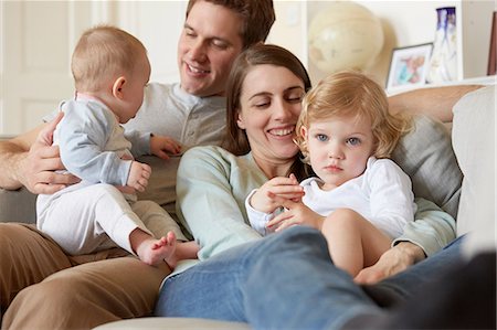 simsearch:649-08422552,k - Mid adult parents huddled on sofa with baby and toddler daughter Foto de stock - Sin royalties Premium, Código: 649-08901022