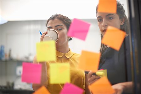 simsearch:614-06718107,k - Two businesswomen drinking coffee and staring at sticky notes on office glass wall Stock Photo - Premium Royalty-Free, Code: 649-08901450