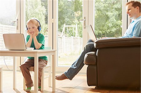 Boy at desk and father on sofa using laptops Stock Photo - Premium Royalty-Free, Code: 649-08901462