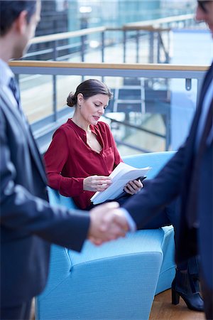 report (written account) - Businessmen shaking hands looking at businesswoman reading paperwork in office atrium Stock Photo - Premium Royalty-Free, Code: 649-08924382