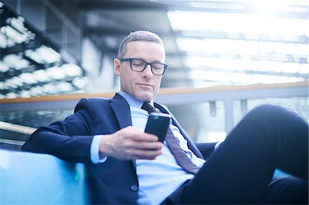 simsearch:649-07520071,k - Businessman on sofa looking at smartphone in office atrium Stock Photo - Premium Royalty-Free, Code: 649-08924390