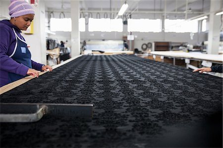 Factory workers smoothing black patterned textile on work table in clothing factory Stock Photo - Premium Royalty-Free, Code: 649-08922790