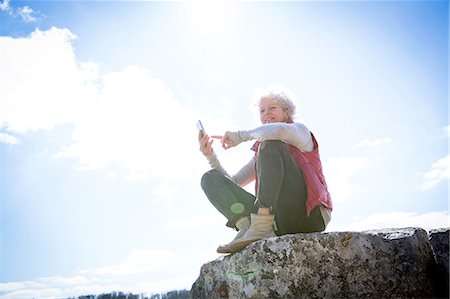 Woman sitting on rock holding smartphone smiling, Bruniquel, France Stock Photo - Premium Royalty-Free, Code: 649-08923321