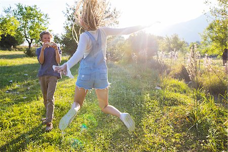Fun young woman jumping in field being photographed by boyfriend, Majorca, Spain Stock Photo - Premium Royalty-Free, Code: 649-08951037
