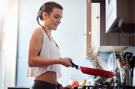 Young woman drinking tossing toasted nuts at kitchen hobs Stock Photo - Premium Royalty-Free, Code: 649-08969596