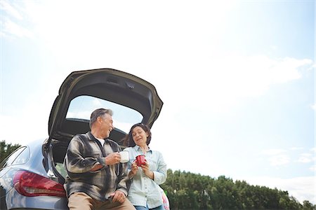 Mature couple standing beside car, holding tin cups, smiling, low angle view Stock Photo - Premium Royalty-Free, Code: 649-09025707