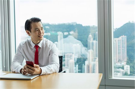 simsearch:649-07520071,k - Business man at desk with smartphone looking away smiling Stock Photo - Premium Royalty-Free, Code: 649-09035465