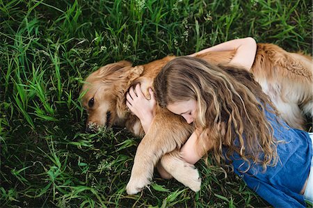 Overhead view of girl lying on grass hugging golden retriever dog Stock Photo - Premium Royalty-Free, Code: 649-09035545