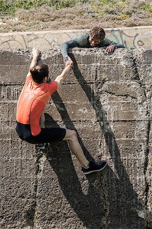 simsearch:6122-08212737,k - Young male free climber at top of sea wall helping friend climb up Stock Photo - Premium Royalty-Free, Code: 649-09035638
