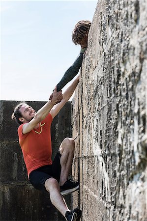 simsearch:6122-08212737,k - Young male free climber at top of sea wall helping friend climb up Stock Photo - Premium Royalty-Free, Code: 649-09035639