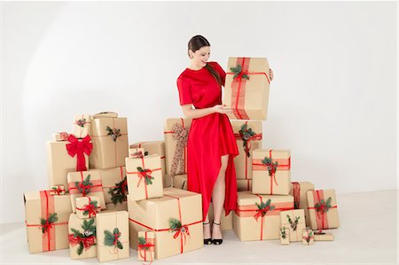 simsearch:649-08085108,k - Young woman in red dress by stacked christmas gifts holding christmas parcel Stock Photo - Premium Royalty-Free, Code: 649-09035864