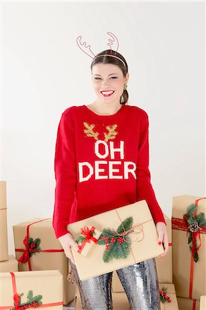 simsearch:649-08085108,k - Portrait of young woman in red sweater and reindeer antlers by stacked christmas gifts holding christmas parcel Stock Photo - Premium Royalty-Free, Code: 649-09035869