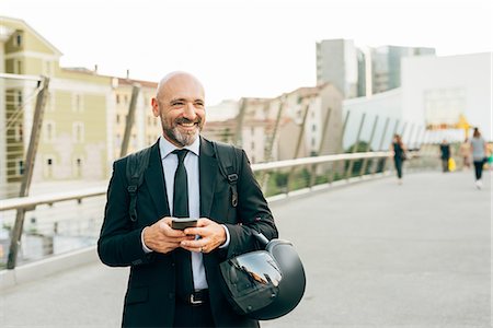 Mature businessman standing on bridge, holding smartphone and motorcycle helmet Stock Photo - Premium Royalty-Free, Code: 649-09061348