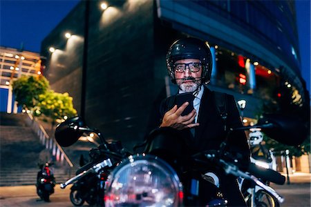 Mature businessman outdoors at night, sitting on motorcycle, using smartphone Stock Photo - Premium Royalty-Free, Code: 649-09061365