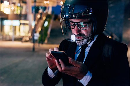 Mature businessman outdoors at night, wearing motorcycle helmet, using smartphone Stock Photo - Premium Royalty-Free, Code: 649-09061366