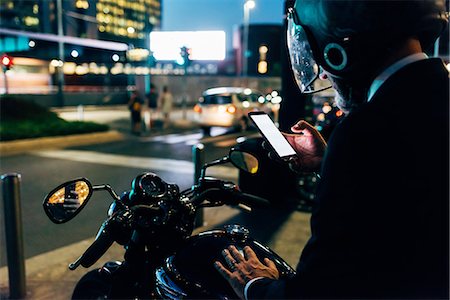 Mature businessman outdoors at night, sitting on motorcycle, wearing motorcycle helmet, using smartphone, rear view Stock Photo - Premium Royalty-Free, Code: 649-09061368