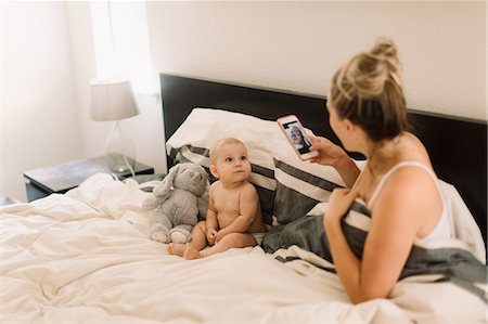 Mother taking smartphone photograph of baby daughter sitting up in bed with soft toy Stock Photo - Premium Royalty-Free, Code: 649-09111513