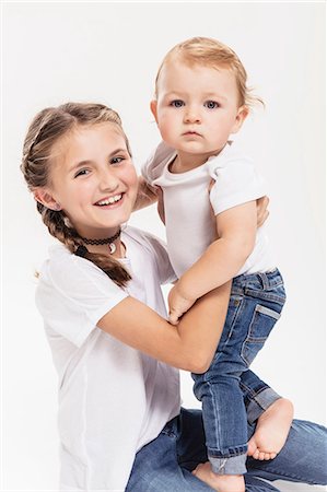 Studio portrait of kneeling girl holding baby brother Stock Photo - Premium Royalty-Free, Code: 649-09111647