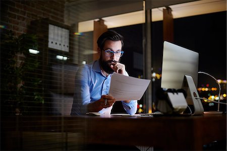 Young businessman reading paperwork at office desk at night Stock Photo - Premium Royalty-Free, Code: 649-09124004