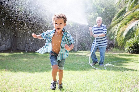 Boy running away from grandfather spraying hosepipe in garden Stock Photo - Premium Royalty-Free, Code: 649-09123646