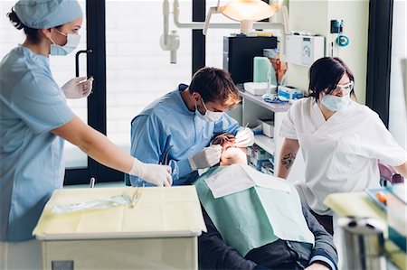 simsearch:649-07709952,k - Dentist looking into male patient's mouth, dental nurses preparing equipment Stock Photo - Premium Royalty-Free, Code: 649-09138870