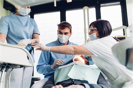 simsearch:649-07709952,k - Dentist looking into male patient's mouth, dental nurses preparing equipment Stock Photo - Premium Royalty-Free, Code: 649-09138871