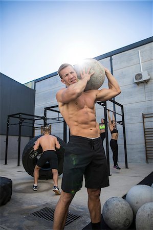 fitness gym male and female intense - Four people exercising in gymnasium, man in foreground using atlas stone Stock Photo - Premium Royalty-Free, Code: 649-09139158