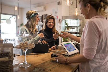 Two female friends, standing at counter in cafe, handing credit card to shop assistant for payment Stock Photo - Premium Royalty-Free, Code: 649-09156222