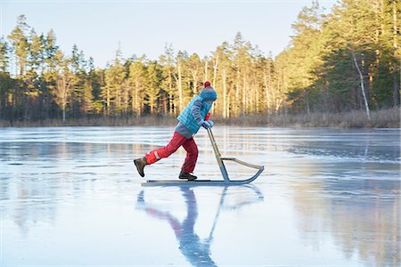 Boy skating on sleigh across frozen lake Foto de stock - Sin royalties Premium, Código: 649-09166459