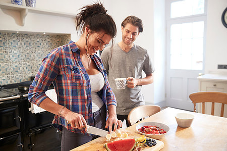 simsearch:649-07761247,k - Couple chatting while slicing fresh fruit at kitchen table Stock Photo - Premium Royalty-Free, Code: 649-09182386