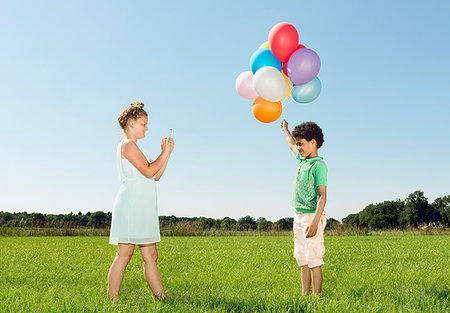simsearch:649-07804673,k - Girl taking smartphone photograph of boy holding bunch of balloons in field Photographie de stock - Premium Libres de Droits, Code: 649-09208906