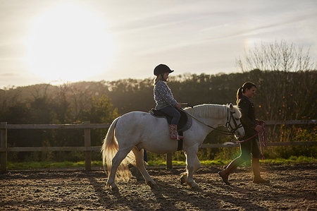 Instructor leading girl riding pony in equestrian arena Stock Photo - Premium Royalty-Free, Code: 649-09209424