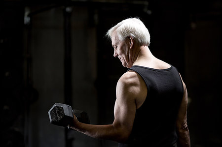 simsearch:693-05552857,k - Senior man doing bicep curls with dumbbell in dark crossfit gym Stock Photo - Premium Royalty-Free, Code: 649-09209645