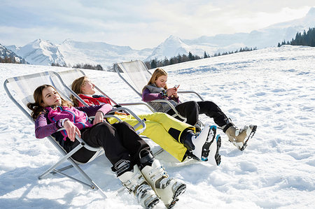 Three teenage girl skiers sitting in deck chairs in snow covered landscape, Tyrol, Styria, Austria Stock Photo - Premium Royalty-Free, Code: 649-09257317