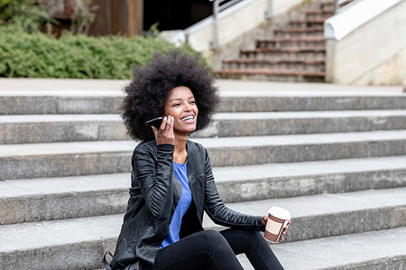 simsearch:614-09078761,k - Happy young woman with afro hair sitting on city stairway, listening to smartphone Stock Photo - Premium Royalty-Free, Code: 649-09257707