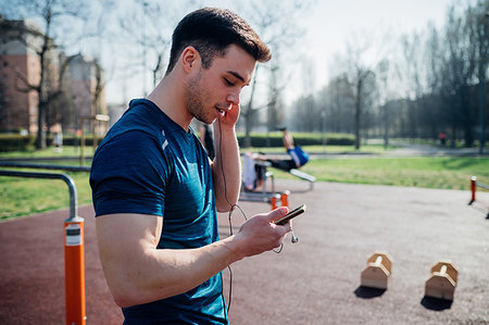 simsearch:693-07672615,k - Calisthenics at outdoor gym, young man listening to earphone and looking at smartphone Stock Photo - Premium Royalty-Free, Code: 649-09257974