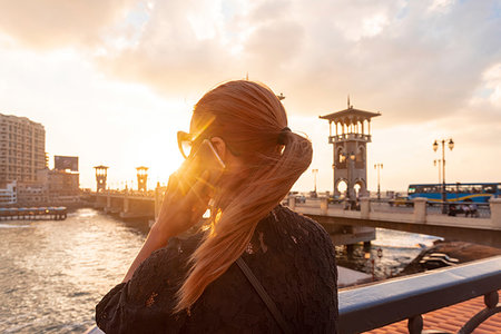 Female tourist with red hair making smartphone call near Stanley bridge at sunset, rear view, Alexandria, Egypt Stock Photo - Premium Royalty-Free, Code: 649-09250316