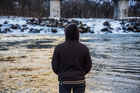 simsearch:649-08924209,k - Young man in hood looking out at winter river, rear view, Domodossola, Piemonte, Italy Stock Photo - Premium Royalty-Free, Code: 649-09251794