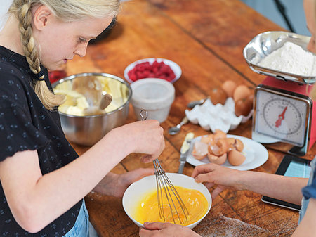 simsearch:614-06897440,k - Girl and her sister baking a cake, whisking eggs in a bowl at kitchen table Stock Photo - Premium Royalty-Free, Code: 649-09276193