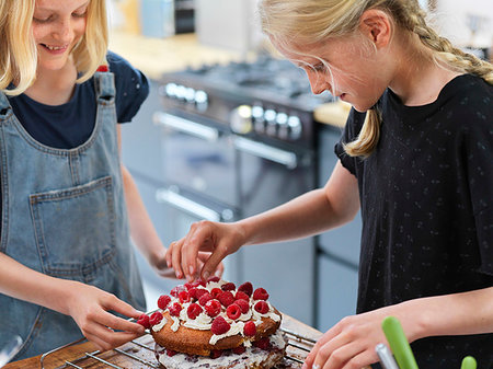 simsearch:614-06897440,k - Girl and her sister baking a cake, decorating cake with fresh cream and raspberries at kitchen table Stock Photo - Premium Royalty-Free, Code: 649-09276210