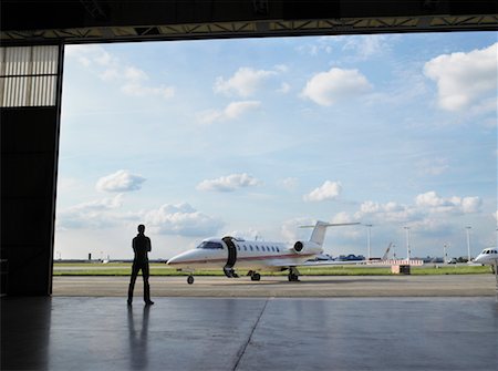 servicing a plane - Technician in hangar looking at private jet on tarmac. Stock Photo - Premium Royalty-Free, Code: 649-01608700