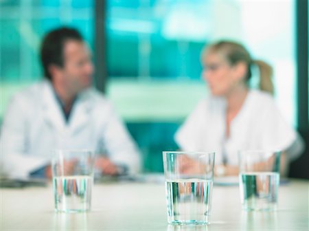 Two doctors in a business meeting. Out of focus. Close up on glasses of water in foreground. Stock Photo - Premium Royalty-Free, Code: 649-01608857