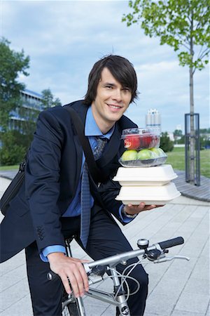 Businessman in park on bike with lots of lunchboxes laughing. Stock Photo - Premium Royalty-Free, Code: 649-01609822