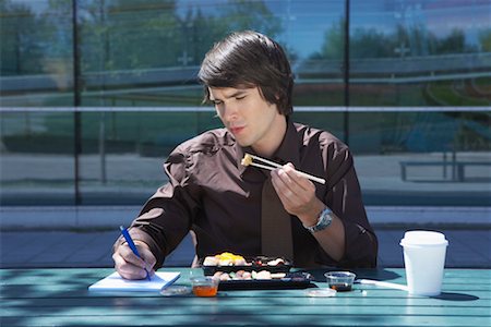 Businessman eating sushi outside while making notes. Stock Photo - Premium Royalty-Free, Code: 649-01609858