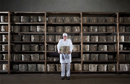 refinery - Man holding large cheese in front of rack of cheese. Stock Photo - Premium Royalty-Free, Code: 649-01610654